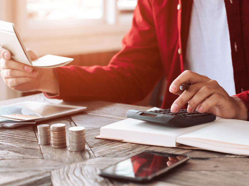 Beitragsbild zum Ratgeber Deckungsbeitragsrechnung. Mensch sitzt am Tisch und rechnet auf dem Taschenrechner