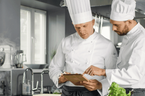Zwei Köche in der Hotellerie geben Bestellungen über ein Tablet auf